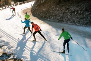 Team of young people cross country skiing training on a winding mountain road in colorful ski clothes