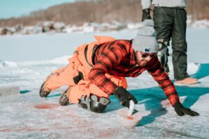 Man in orange jump suit kneels and hits curling stone