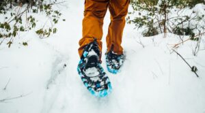 Man in orange trousers snow shoeing through winter landscape